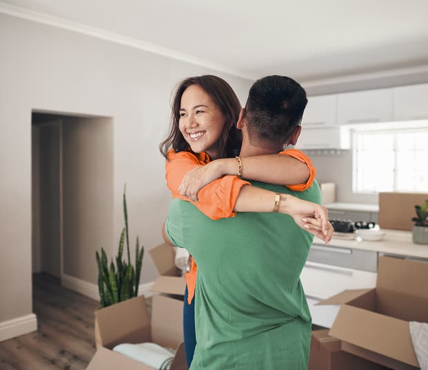 A happy couple hugging in a living room filled with moving boxes