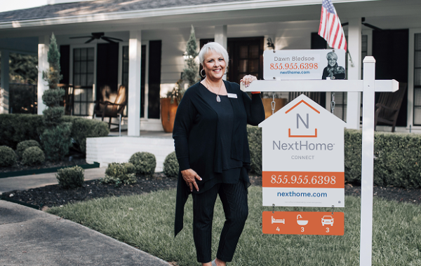 A woman standing next to a NextHome for sale sign